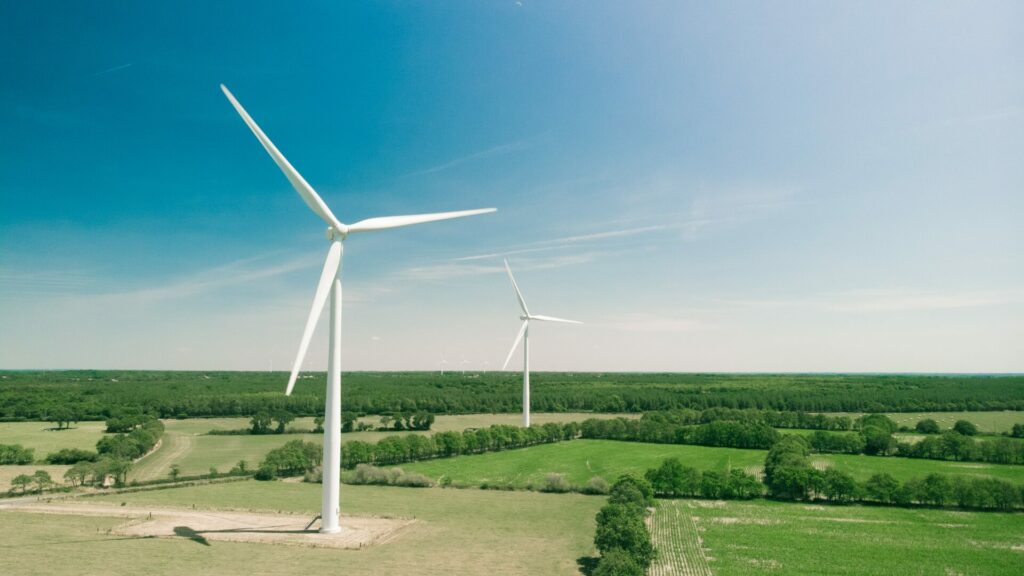 Landscape photo of two white wind turbines in a field, accompanied by a blue sky.